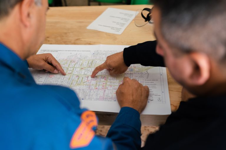 zdjęcie przedstawia dwóch mężczyzn analizujących plany budowlane umieszczone na arkuszu papieru