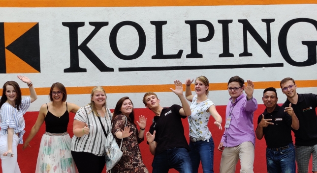 zdjęcie przedstawia młodych ludzi w kolorowych strojach na tle logo KOLPING
